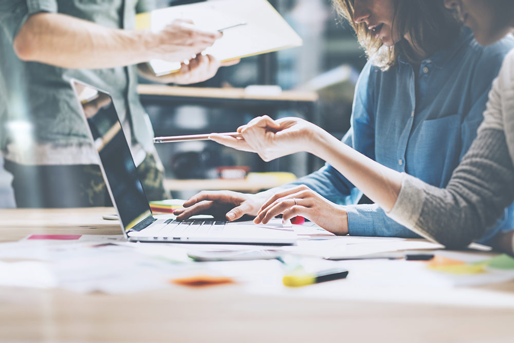 Digital marketing team looking at computer and one person pointing at laptop screen