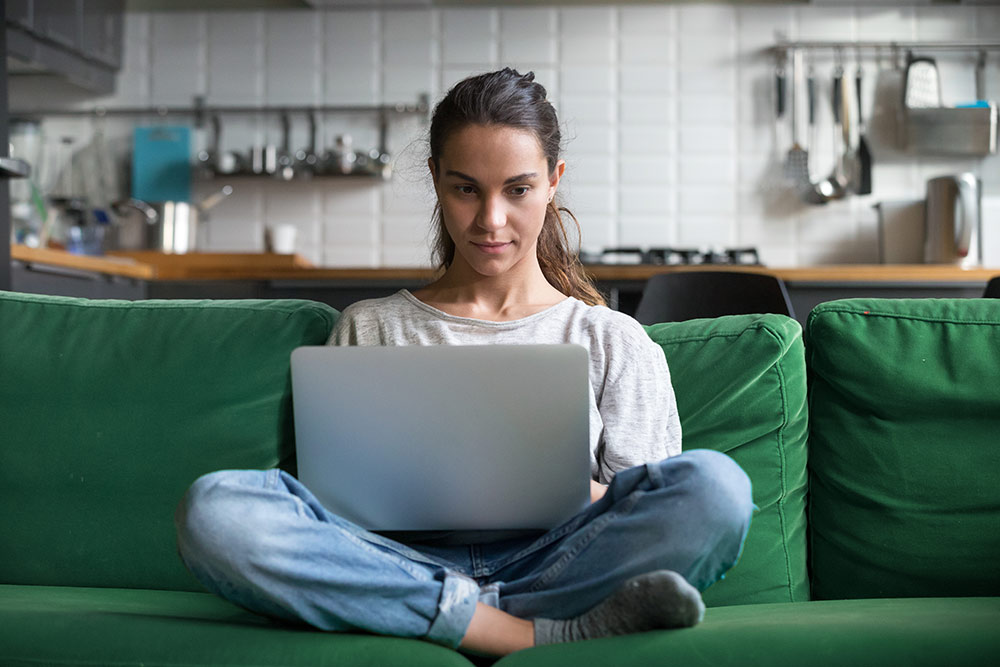 Woman sitting on green couch with laptop in lap