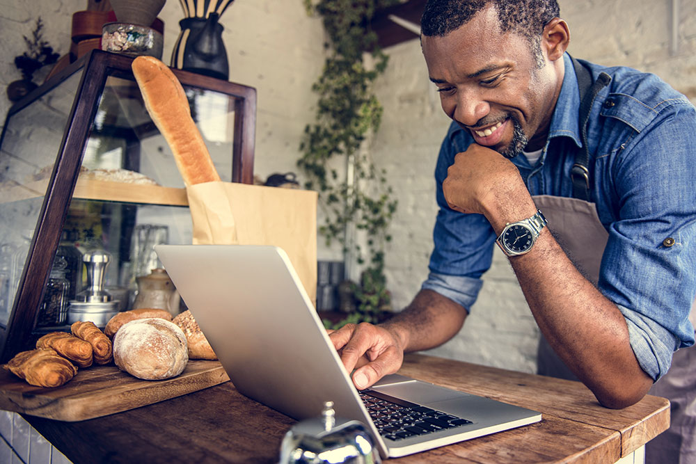 Baker on laptop in shop smiling