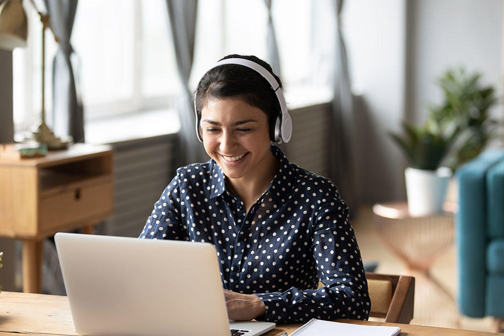 Woman sitting at laptop with headphones on watching video