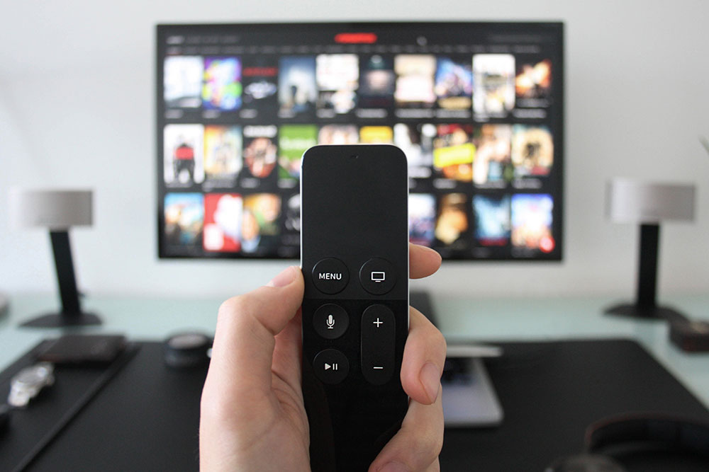 Close up of person holding remote with tv on in background with Netflix menu on screen