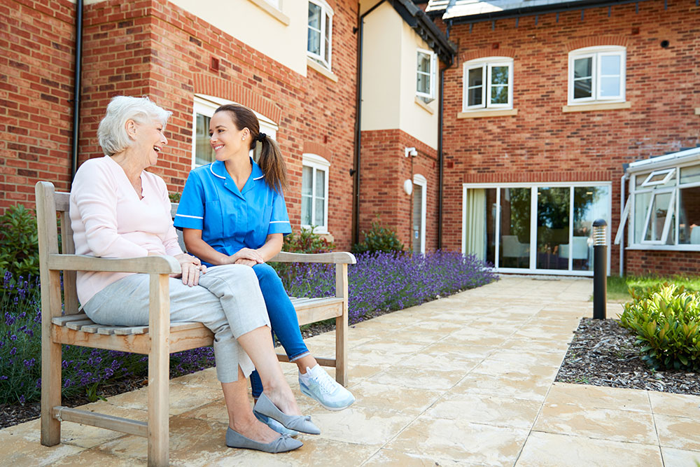 Senior woman sitting with caregiver in senior community sitting on bench