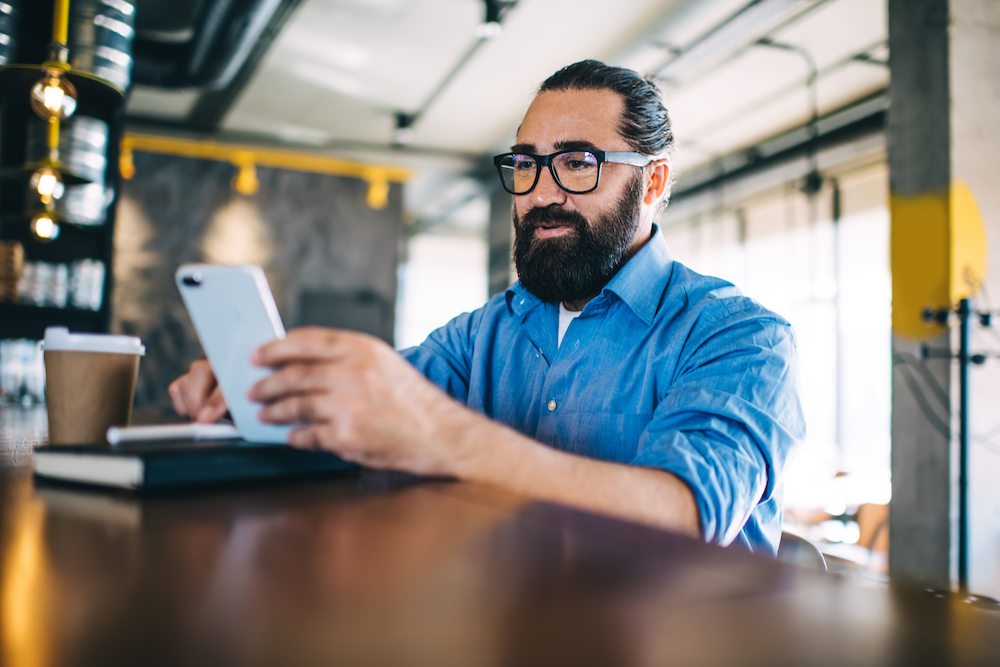 A coffee shop owner does social media marketing on his phone