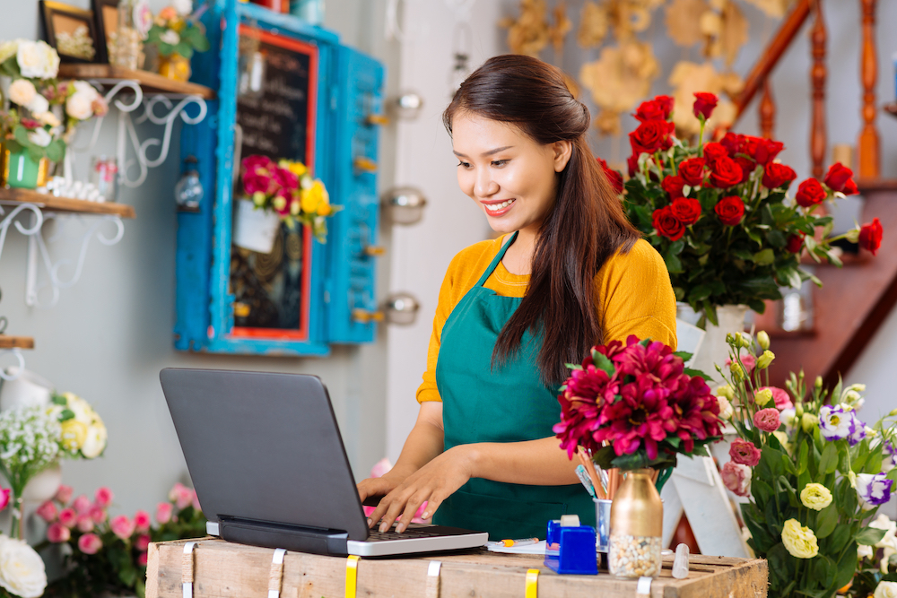 A flower business owner uses her computer to manage social media