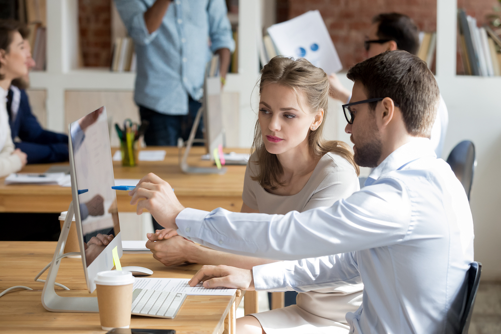 Two marketing employees pointing at a screen and discussing strategy