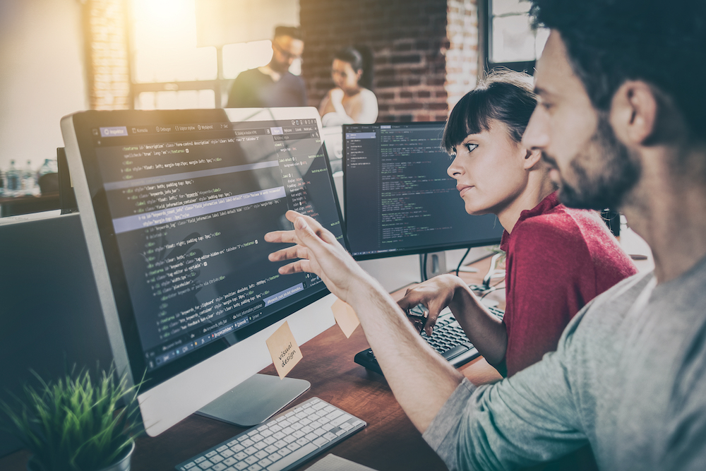 Two members of a web design services team work together to code a website