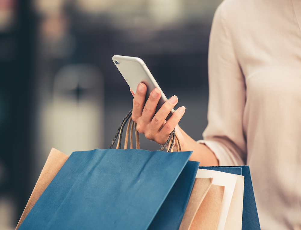 A young woman using her cell phone while holding shopping bags