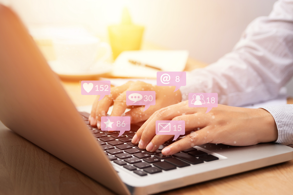 A woman typing on her computer while engaging with social media