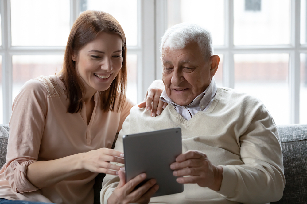 A senior man and his daughter look at social media on their tablet 