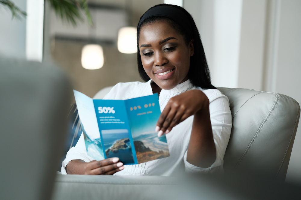 A smiling young woman reviews a travel brochure