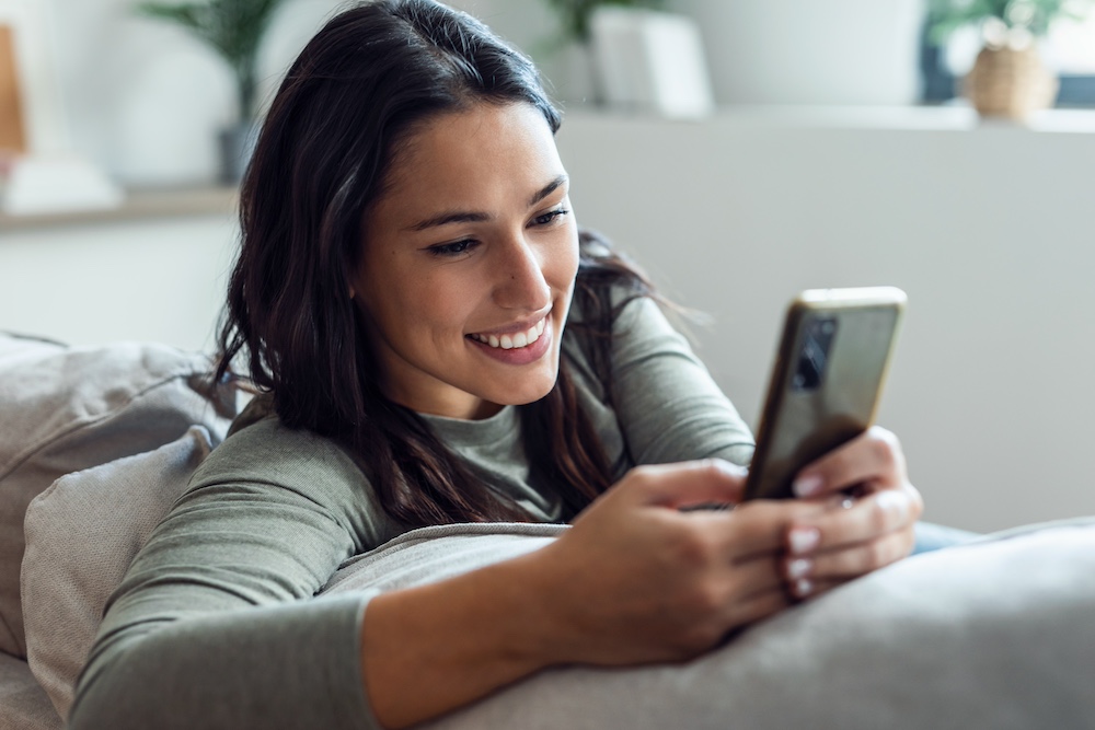 A smiling woman using her phone while sitting in her living room