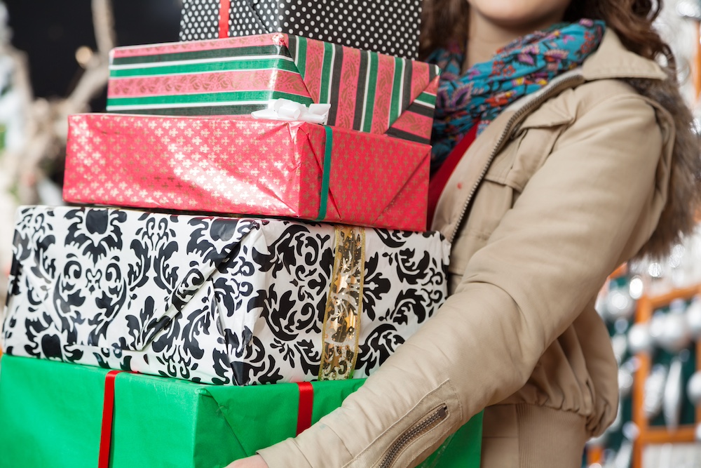 A woman carrying a large stack of Christmas gifts
