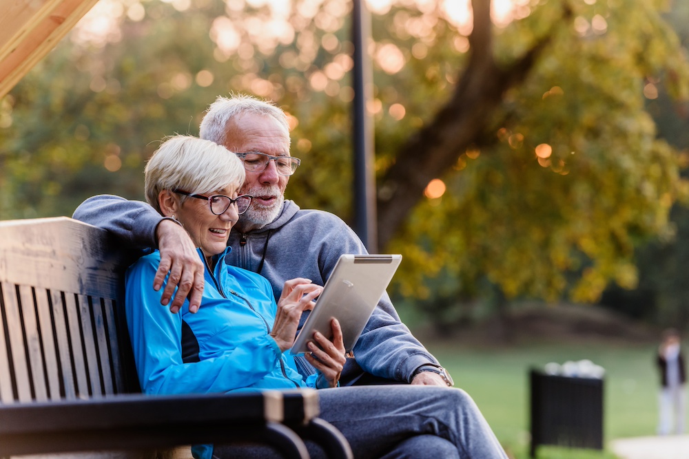 An older couple reads a blog on their tablet while sitting outdoors. The blog was written by senior living marketing services