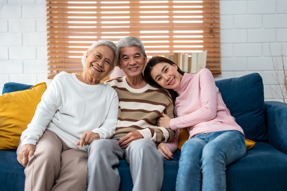 Senior parents with adult daughter sitting on couch of memory care community they found using Memory Care Marketing